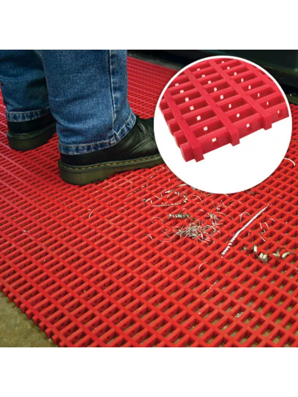 Anti-slip modular floor matting in red with drainage holes, shown underfoot in an industrial environment.
