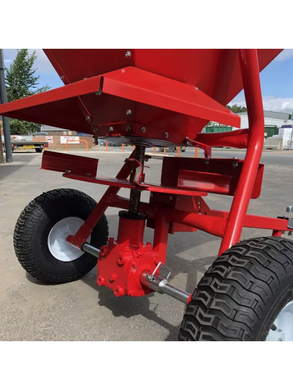 Underside view of red fertiliser spreader with heavy-duty tyres and spreading system for even ground coverage.