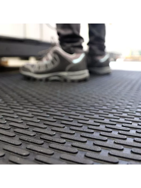 Anti-slip rubber mat with raised surface pattern, shown under safety footwear in an industrial setting.