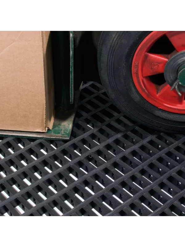 Heavy-duty black floor mat supporting a pallet and trolley wheel in a warehouse setting.