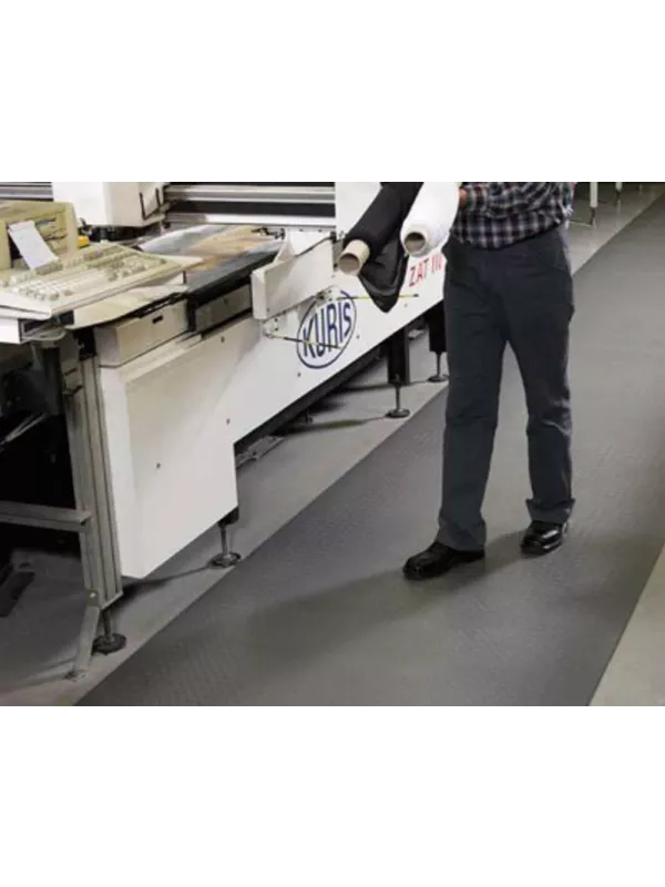 Worker standing on anti-fatigue mat beside machinery – cushioned floor mat for workplace comfort and safety.